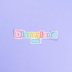 May include: A colorful sticker with the text "Disneyland Paris" in white letters on a rainbow background.