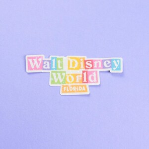 May include: A colorful sticker with the text "Walt Disney World" in a retro font. The words are in individual boxes with different colors. The text "Florida" is in a smaller box below the main text.