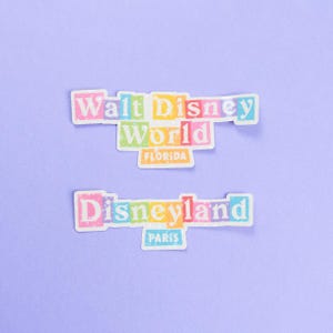 May include: Two colourful stickers with the text "Walt Disney World Florida" and "Disneyland Paris" on a light purple background.