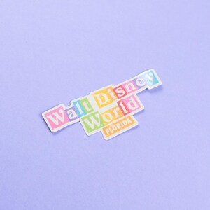 May include: A colorful sticker with the text "Walt Disney World" and "Florida" in white letters. The sticker is on a light purple background.