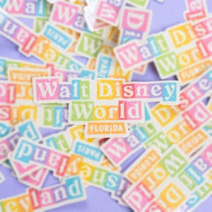 May include: A collection of colorful stickers featuring the Walt Disney World logo. The stickers are arranged in a random pattern on a purple background. The main sticker in the center reads "Walt Disney World Florida".