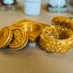 May include: A set of gold-colored resin grinder and a small box with a lid. The grinder has a textured surface and the box has a glittery finish.