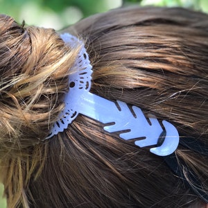 May include: A white plastic mask extender with a decorative lace design. The extender is attached to a black elastic band.