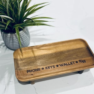 May include: A wooden tray with four legs, engraved with the words "PHONE • KEYS • WALLET • KISS".
