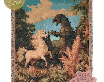 May include: A tapestry throw blanket featuring a green Godzilla-like monster facing a white unicorn in a forest setting. The blanket has a fringed edge and a label that reads "Ultra Soft Cozy".