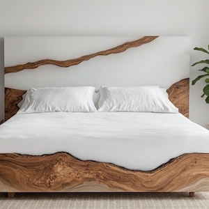 May include: A contemporary bed featuring a distinctive design. The headboard and frame are crafted from wood, showcasing a natural grain. The headboard incorporates a white epoxy resin inlay with a brown wood grain pattern. The bed is dressed with white linens.