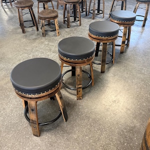 May include: A collection of bar stools featuring circular black padded seats with silver nailhead trim. The bases are constructed from curved wooden barrel staves with black metal circular footrests, providing a sturdy structure for each stool.