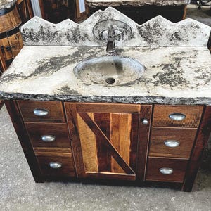 May include: A rustic bathroom vanity with a concrete countertop and a single sink. The vanity has a wooden cabinet with four drawers and a single door. The door is made of reclaimed wood with a unique pattern.