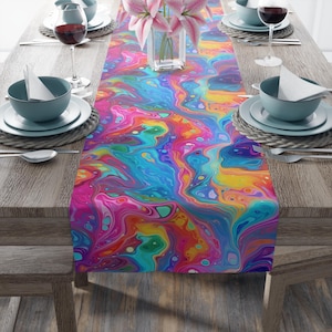 May include: A vibrant, colorful table runner with a fluid, abstract design. The runner features a swirling pattern of pink, blue, yellow, and green hues. The table is set with plates, bowls, silverware, and wine glasses, creating a dining setting.