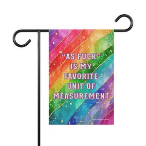 May include: A colorful garden flag with a rainbow design and the text "AS FUCK IS MY FAVORITE UNIT OF MEASUREMENT". The flag is mounted on a black metal stand.