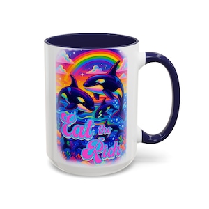 May include: White ceramic mug with a navy blue interior and handle. The mug features a colourful illustration of orcas swimming in the ocean under a rainbow. The text "Eat the Rich" is displayed in a pink, retro font.