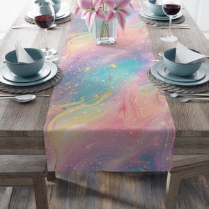 Puede incluir: Un camino de mesa colorido con un diseño de mármol pastel. El camino de mesa presenta tonos de rosa, azul y amarillo con detalles dorados. La mesa está puesta con platos, cubiertos y copas de vino, creando una escena elegante.