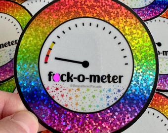 May include: Round sticker with a rainbow glitter border and a white face. The text "fuck-o-meter" is printed in black, with a needle pointing to the red zone. The sticker has a gauge design and the text "@BespatteredFacade".