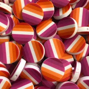 May include: A collection of round, flat beads in shades of orange, white, and pink, arranged in a pile. Each bead features a striped design, with the colors arranged in horizontal bands. The beads have a smooth, glossy finish and are likely made of plastic or resin.