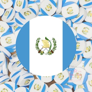 May include: A collection of white, blue, and yellow round objects, many with a Guatemalan flag design. The central focus is a large circle with the Guatemalan flag, featuring a bird, scroll, and crossed weapons. The objects are scattered across a wooden surface.