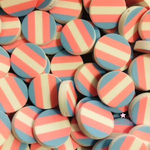 May include: A collection of round, flat, decorative items with a transgender pride flag design. Each item features alternating stripes of light blue, pink, and white. The items are arranged in a close-up, scattered pattern.