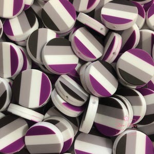 May include: A collection of round, flat beads in the colors of the asexual pride flag: purple, gray, white, and black. The beads are striped and have a hole for stringing. The beads are made of a smooth, possibly silicone material.