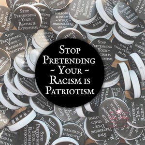 以下が含まれることがあります： 「Stop Pretending - Your - Racism Is Patriotism」と白い文字で書かれた丸い灰色のボタンのコレクション。中央の大きな黒い円がメッセージを繰り返しています。ボタンには白い縁があります。