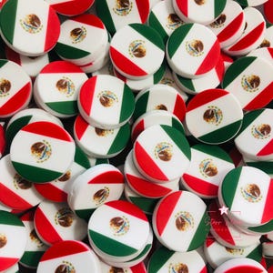 Puede incluir: Un conjunto de objetos redondos y blancos con el diseño de la bandera mexicana. Cada objeto presenta franjas verdes y rojas con el escudo de armas mexicano en el centro. Los objetos están dispersos, creando un patrón visualmente atractivo.