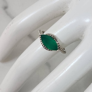 May include: A silver ring with a marquise-shaped green gemstone set in a silver band with a beaded design.