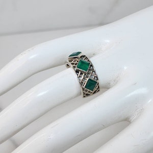 May include: A silver ring with a geometric design and three green gemstones.