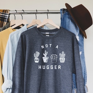 May include: A dark gray sweatshirt with the text "NOT A HUGGER" and a row of four potted cactus illustrations in white.