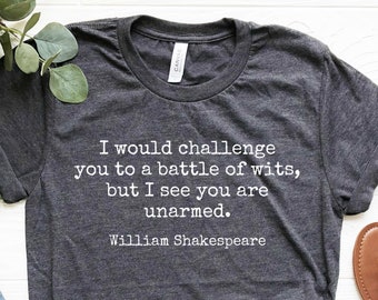May include: A dark gray t-shirt with a white quote from William Shakespeare that reads "I would challenge you to a battle of wits, but I see you are unarmed."