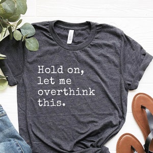 May include: A dark gray t-shirt with the text "Hold on, let me overthink this." printed in white.