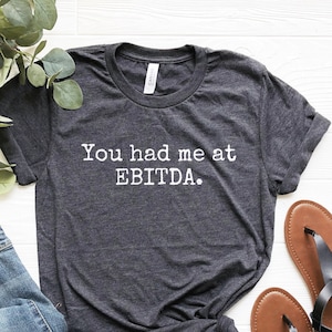May include: A dark gray t-shirt with the text "You had me at EBITDA." printed in white.