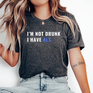 May include: A dark grey heather t-shirt with the text "I'm not drunk I have ALS" in white with the word "ALS" in blue.