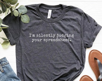 May include: A dark grey t-shirt with the text "I'm silently judging your spreadsheet." printed in white.