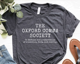 May include: A dark heather grey t-shirt with the text "THE OXFORD COMMA SOCIETY" and the phrase "In defense and preservation of tradition, form, and clarity." printed in white.
