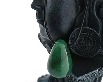 Może przedstawiać: Zielony jadeitowy wisiorek na czarnym skórzanym sznurku zwisa z ucha czarnej kamiennej statuetki Buddy.