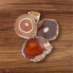 May include: Four agate coasters in shades of brown and orange. The coasters are round and have a natural, polished finish.