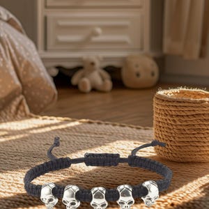 Könnte beinhalten: Ein schwarzes geflochtenes Armband mit silbernen Totenkopfperlen. Das Armband ist verstellbar und hat ein schlichtes Design.