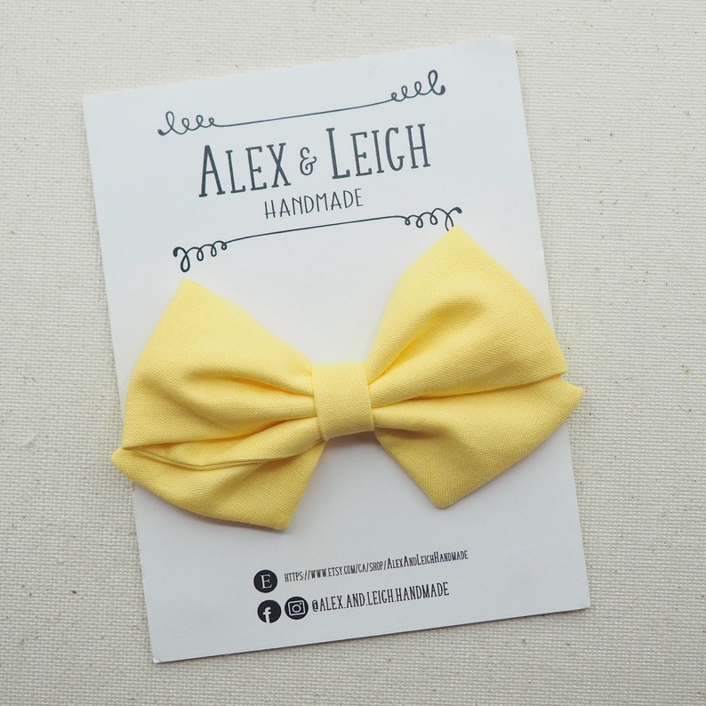 May include: A yellow fabric bow tie on a white card with the text "ALEX & LEIGH HANDMADE" and contact information for the shop.