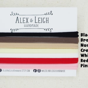 May include: A set of eight hair ties in various colors, including black, brown, nude, cream, white, red, and pink. The hair ties are arranged in a stack, with the colors visible. The text "ALEX & LEIGH HANDMADE" is printed on a white card behind the hair ties.