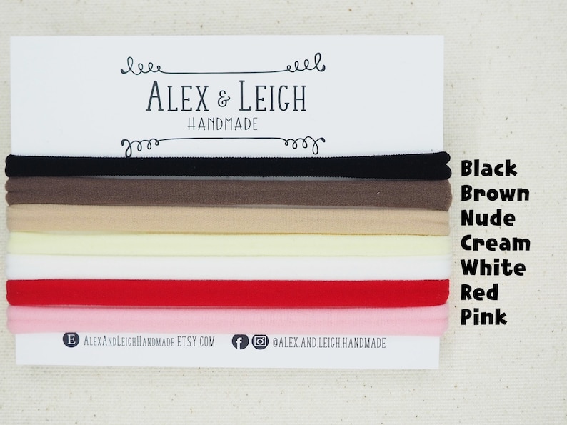 May include: A set of eight hair ties in various colors, including black, brown, nude, cream, white, red, and pink. The hair ties are arranged in a stack, with the colors visible. The text "ALEX & LEIGH HANDMADE" is printed on a white card behind the hair ties.