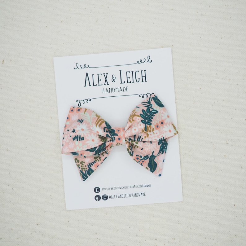 K&ouml;nnte beinhalten: Eine rosa und gr&uuml;ne Blumen Schleife auf wei&szlig;em Hintergrund. Die Schleife ist handgefertigt von Alex & Leigh.