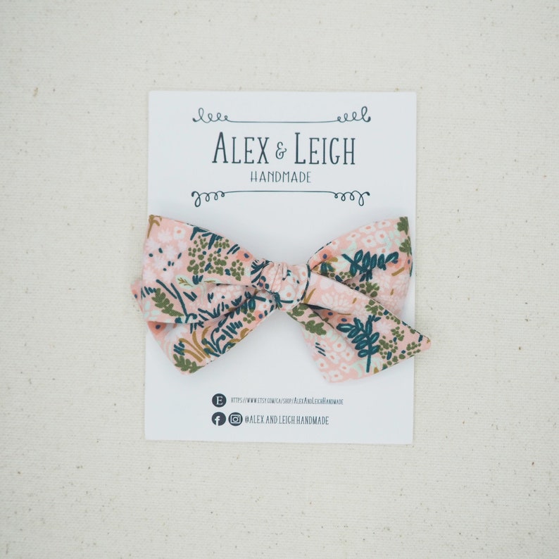 K&ouml;nnte beinhalten: Eine rosa und gr&uuml;ne Blumenstoffschleife auf wei&szlig;em Hintergrund. Die Schleife befindet sich auf einer wei&szlig;en Karte mit dem aufgedruckten Text "Alex & Leigh Handmade".