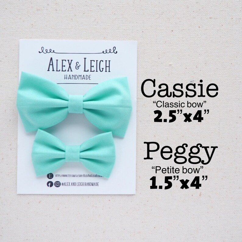 May include: Two handmade fabric bow ties in a light turquoise color. The larger bow tie is labeled "Cassie "Classic bow" 2.5"x4"" and the smaller bow tie is labeled "Peggy "Petite bow" 1.5"x4"".