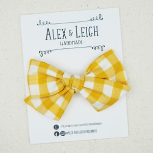 May include: A yellow and white gingham bow with a white card that says "Alex & Leigh Handmade" and includes their website and social media handles.