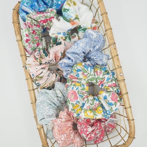 K&ouml;nnte beinhalten: Eine Sammlung bunter Scrunchies mit Blumenmuster in einem goldenen Drahtkorb. Die Scrunchies sind aus Stoff und haben verschiedene Muster, darunter Blumen, Paisley und Punkte.