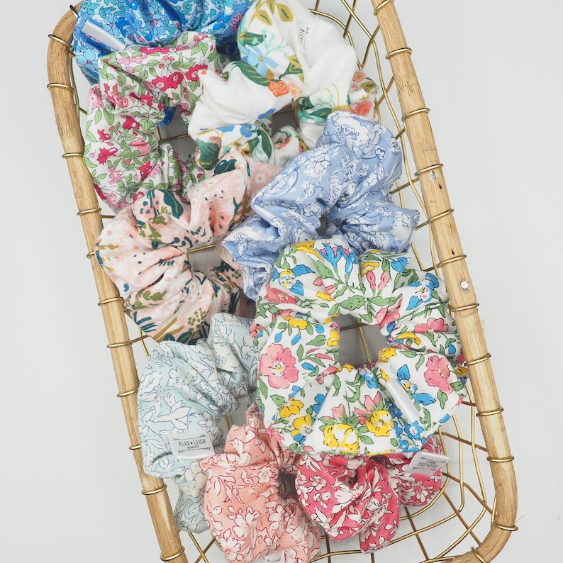 K&ouml;nnte beinhalten: Eine Sammlung bunter Scrunchies mit Blumenmuster in einem goldenen Drahtkorb. Die Scrunchies sind aus Stoff und haben verschiedene Muster, darunter Blumen, Paisley und Punkte.