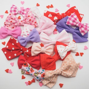 Peut inclure: Un assortiment de n&oelig;uds pour cheveux en tissu faits &agrave; la main dans diff&eacute;rentes couleurs et motifs, notamment des pois rouges, blancs, roses, bleus et noirs. Les n&oelig;uds sont fabriqu&eacute;s avec diff&eacute;rents tissus, tels que le coton et le satin, et sont nou&eacute;s avec un ruban.