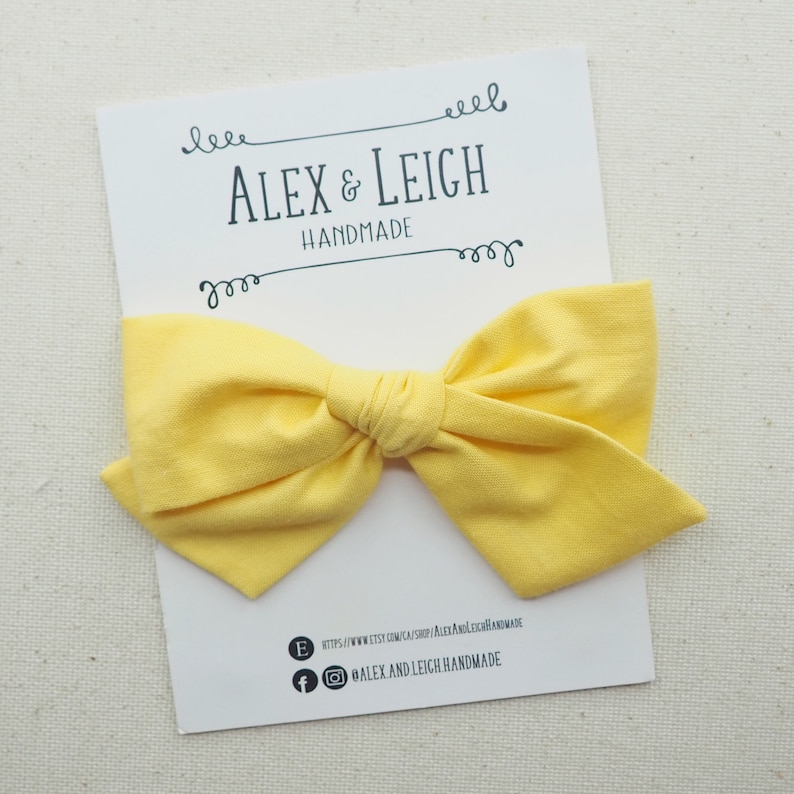 May include: A yellow fabric bow on a white card with the text "ALEX & LEIGH HANDMADE" and contact information for the shop.