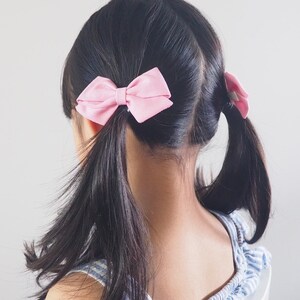 Pu&ograve; includere: Una bambina con lunghi capelli neri che indossa una camicetta blu e bianca a spalle scoperte con due fiocchi rosa nei capelli.