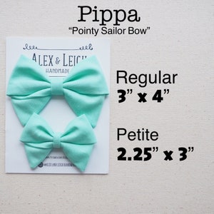 May include: Two aqua blue fabric hair bows, one larger and one smaller. The larger bow is 3 inches by 4 inches and the smaller bow is 2.25 inches by 3 inches. The bows are labeled "Pippa" and "Pointy Sailor Bow".