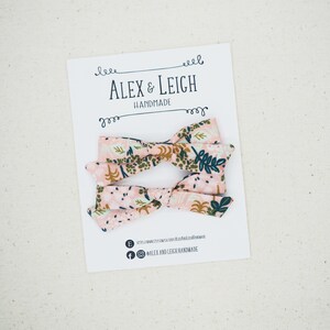 K&ouml;nnte beinhalten: Zwei rosa und gr&uuml;ne florale Stoffhaarb&auml;nder mit wei&szlig;em Hintergrund. Die Schleifen befinden sich auf einer wei&szlig;en Karte mit dem Text "Alex & Leigh Handmade".