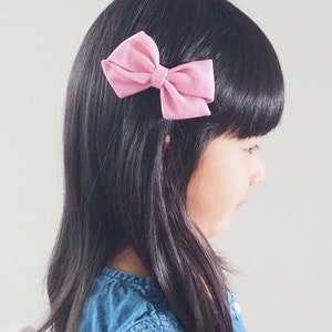 Pu&ograve; includere: Una bambina con lunghi capelli neri che indossa una camicia di jeans blu con un fiocco di stoffa rosa nei capelli.